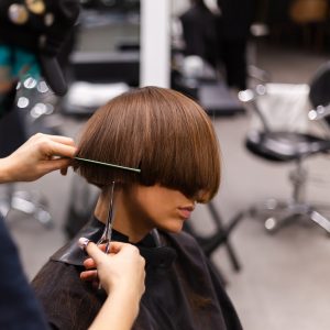 a professional girl hairdresser makes a client haircut. the girl is sitting in a mask in beauty the salon